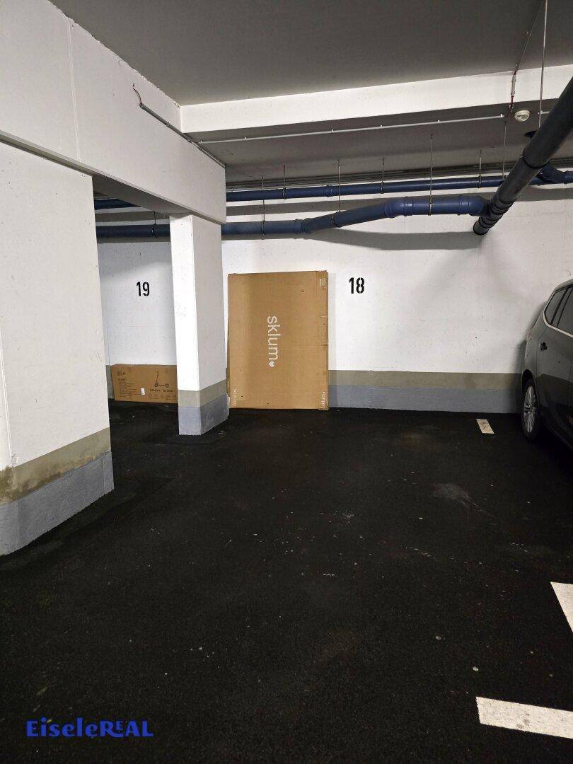 Tiefgaragenstellplatz mit Betonboden und sichtbaren Leitungen, bietet sicheren Parkraum.