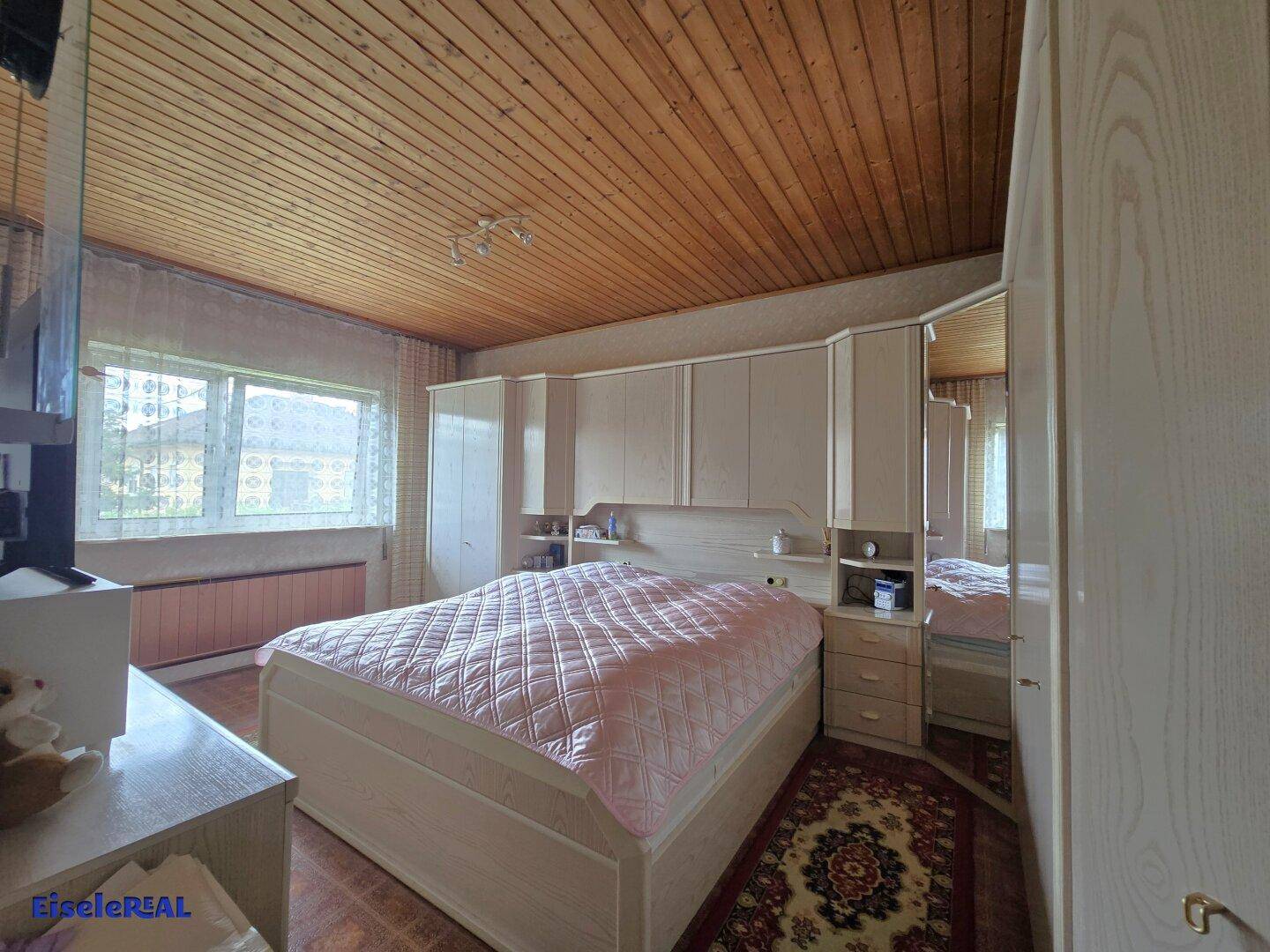 Schlafzimmer mit großem Bett, Einbauschränken und einer Holzpaneeldecke.
