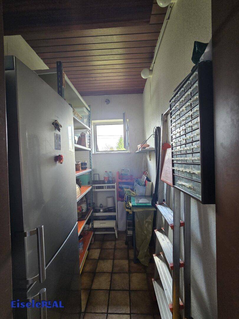 Praktischer Abstellraum mit Regalen, Kühlschrank und Fliesenboden.