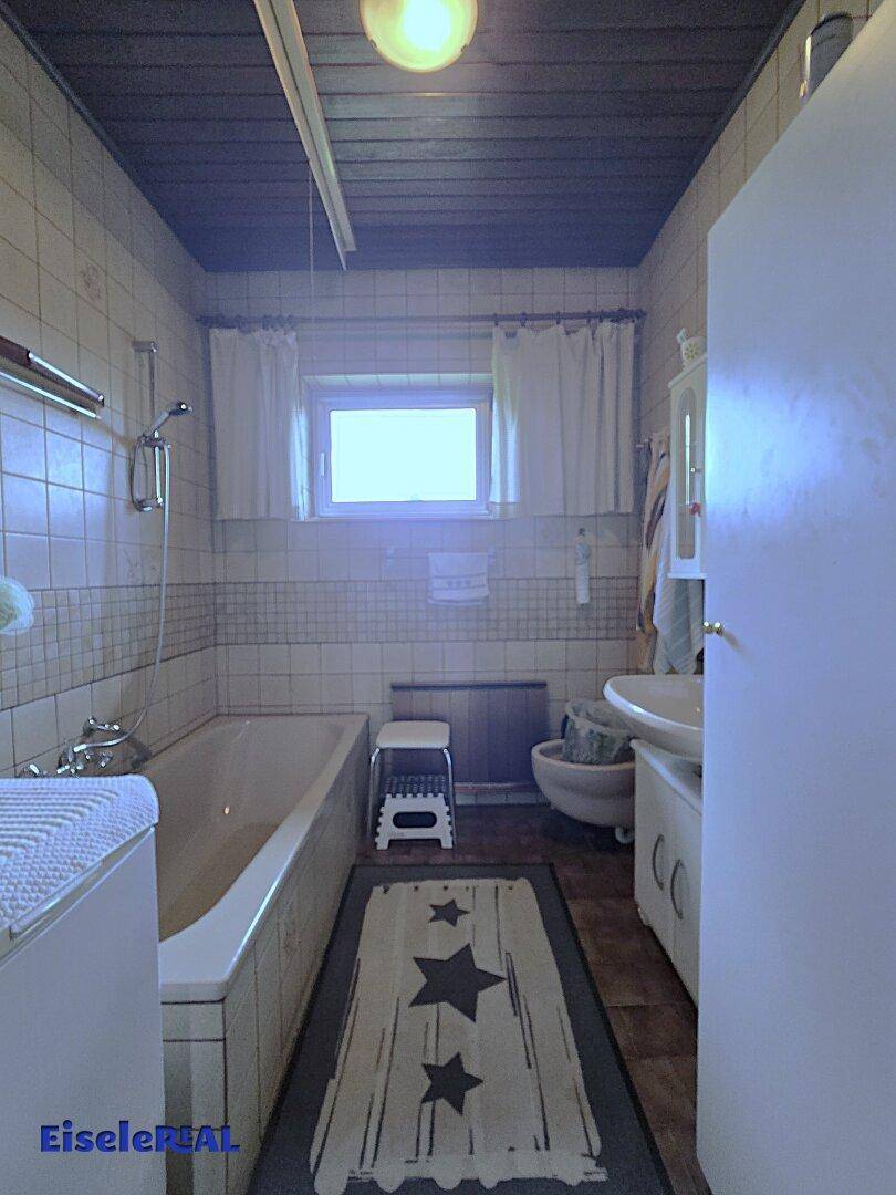 Badezimmer mit Badewanne, Waschbecken, WC und gefliesten Wänden sowie Holzdecke.