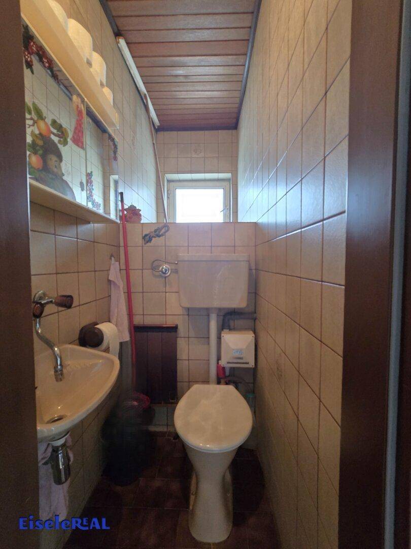 Separates WC mit Toilette, kleinem Waschbecken und gefliesten Wänden sowie Holzdecke.