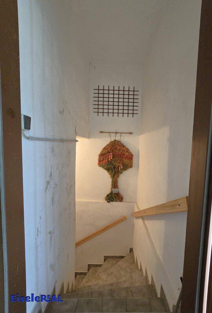 Schlichtes Treppenhaus mit weiß gestrichenen Wänden und Holzhandlauf.