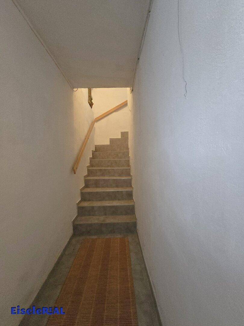 Einfaches Treppenhaus mit weiß gestrichenen Wänden und Teppichläufer.