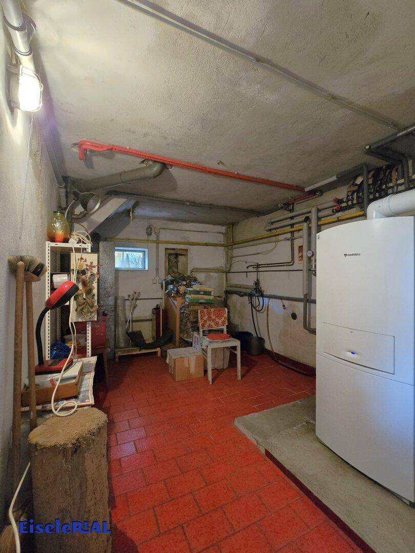 Heizungsraum im Keller mit Heizungsanlage, sichtbaren Rohrleitungen und rotem Fliesenboden.