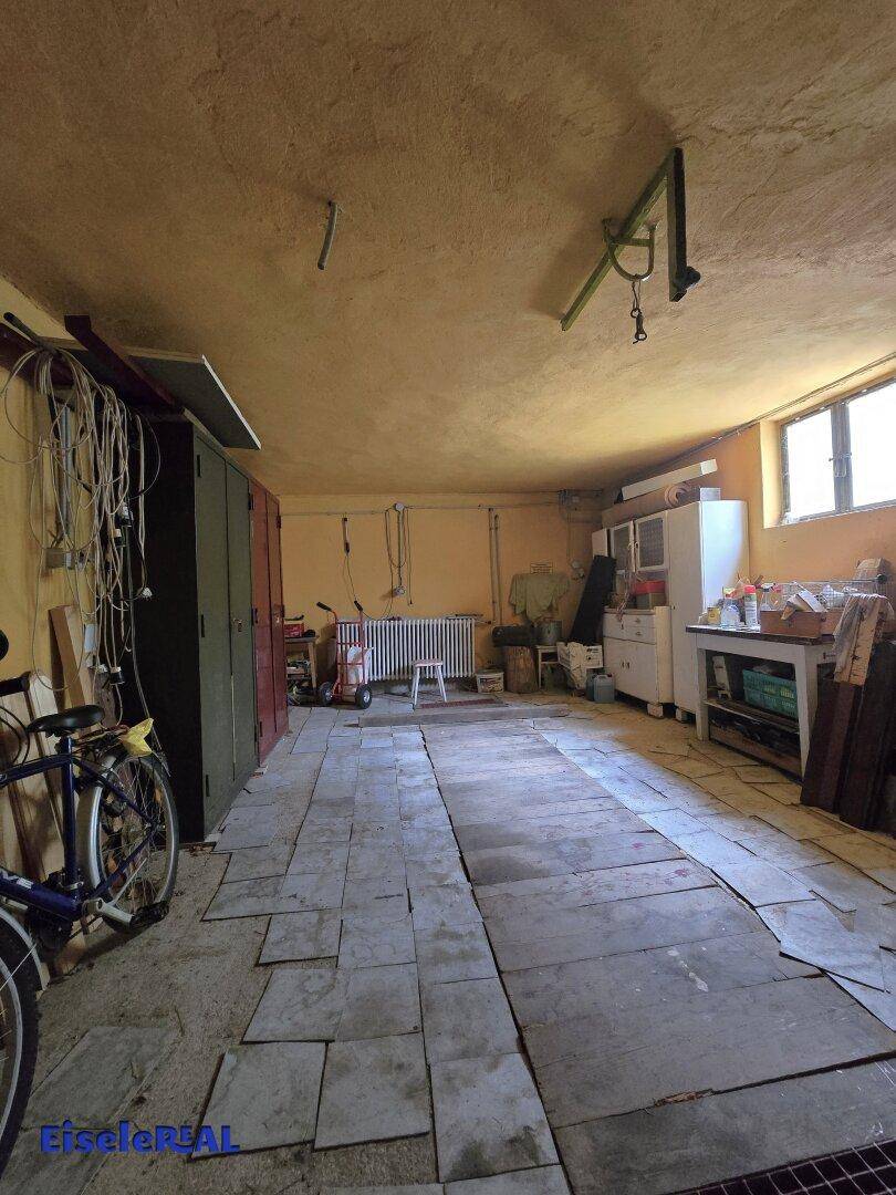 Großer Kellerraum mit provisorischem Boden, Heizkörper und Abstellmöglichkeiten für Fahrräder und Möbel.