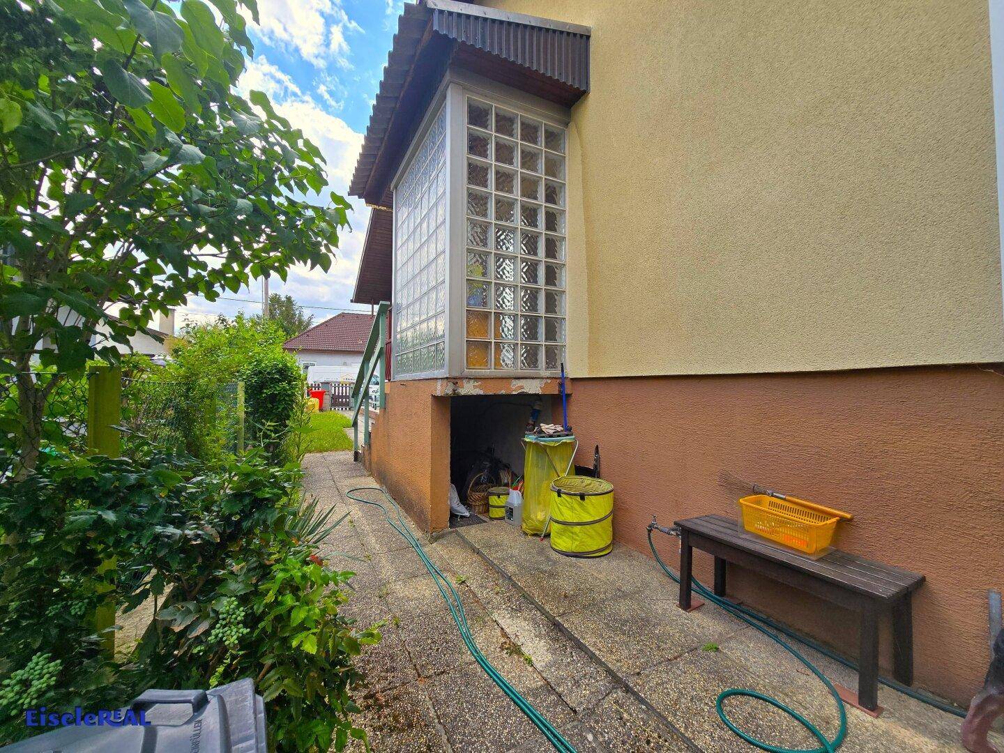 Seitenansicht des Hauses mit Glasbausteinfenster und offenem Lagerbereich im Untergeschoss.