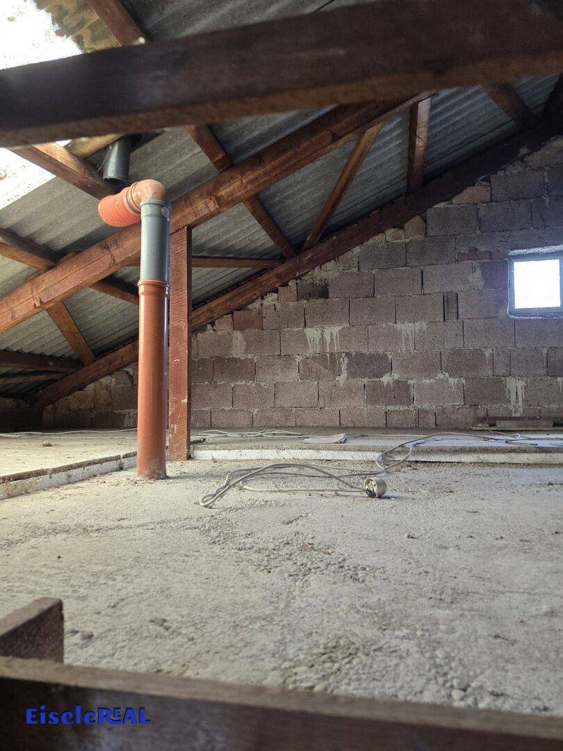 Unausgebauter Dachboden mit unverputzten Wänden, sichtbaren Rohren und Holzbalken, ideal für Lagerung.