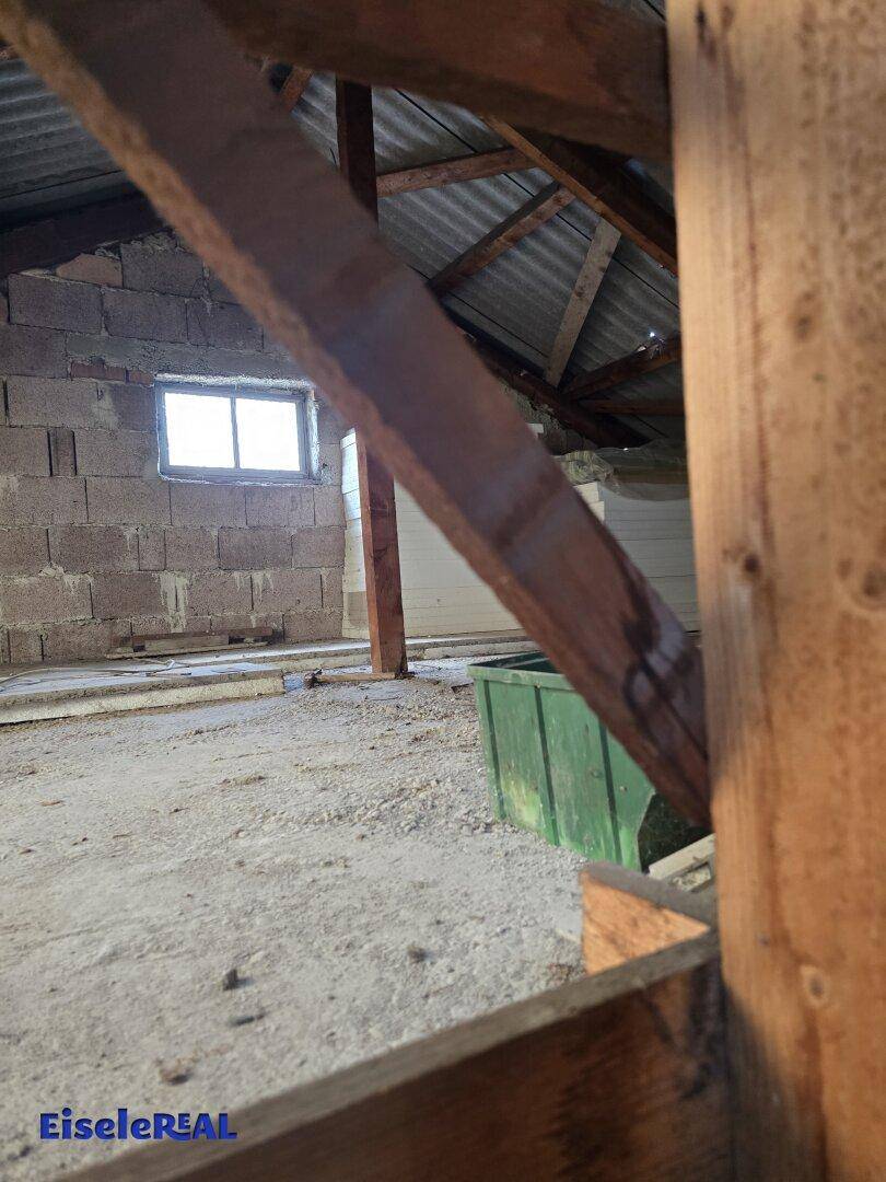 Dachboden mit unverputzten Wänden und einem kleinen Fenster, das Tageslicht in den Lagerbereich bringt.