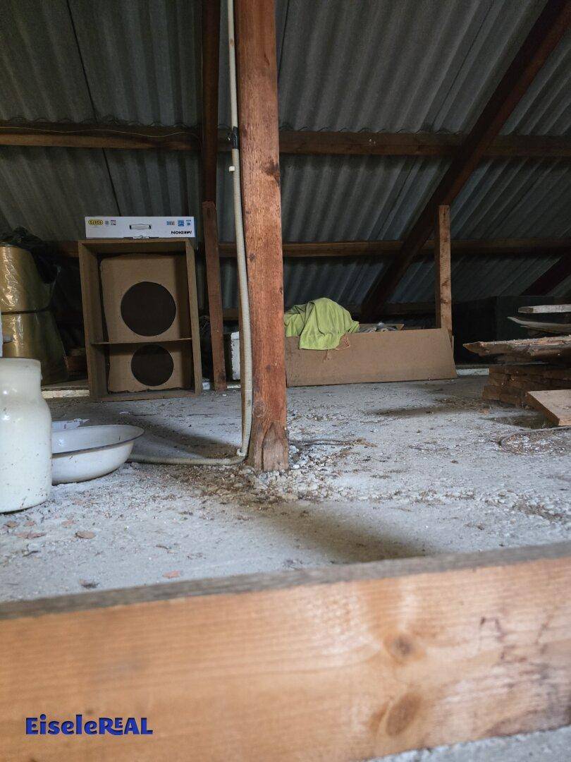 Teil des Dachbodens mit Holzbalken und losem Material auf dem Boden, bereit für eine Renovierung.