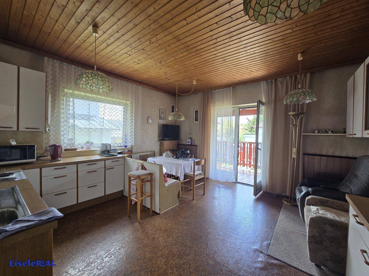 Gemütliche Wohnküche mit Holzdecke, Essbereich und direktem Zugang zum Balkon.