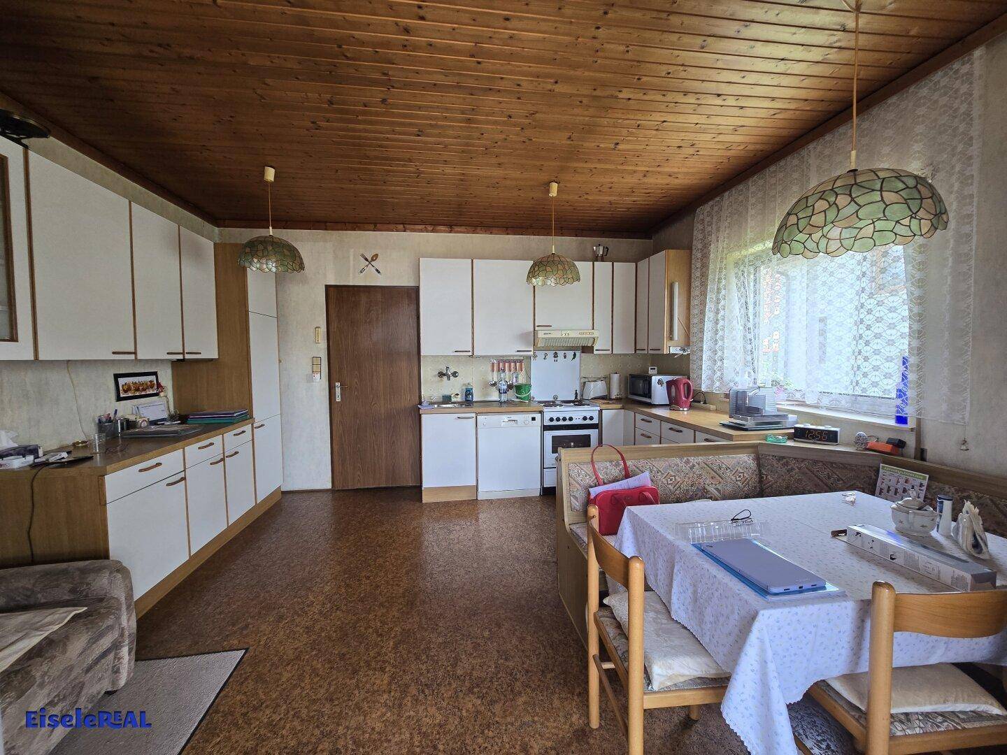 Funktionale Küche mit weißen Schränken, Holzdecke und integriertem Essbereich.