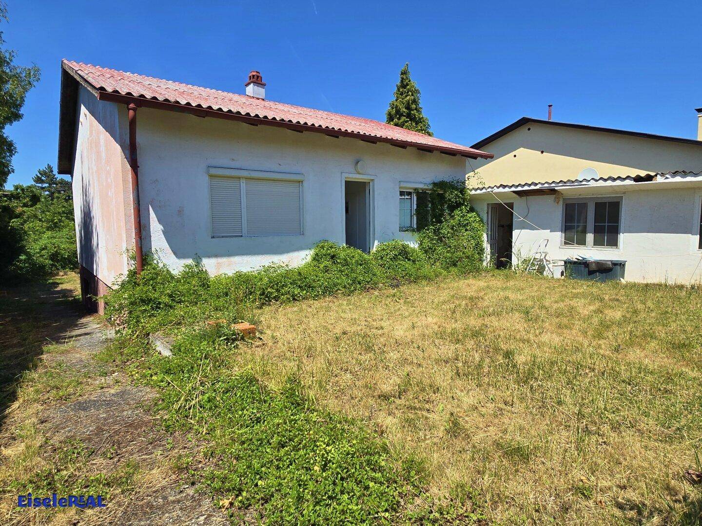 Rückseite des Hauses mit Gartenbereich, bewachsenen Flächen und einem weiteren Gebäude im Hintergrund.