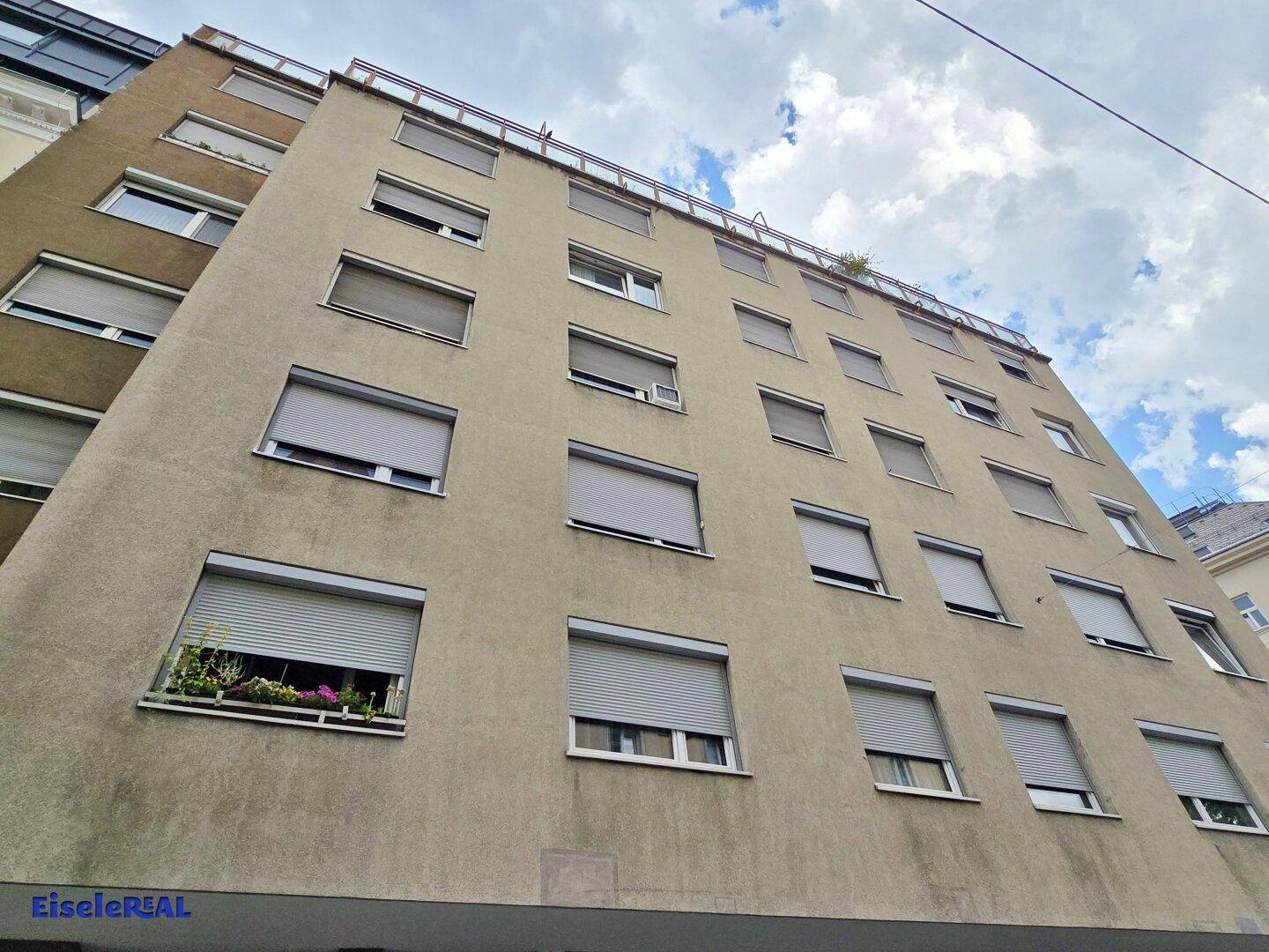 Fassade eines Mehrfamilienhauses mit zahlreichen Fenstern und Rollläden unter bewölktem Himmel.
