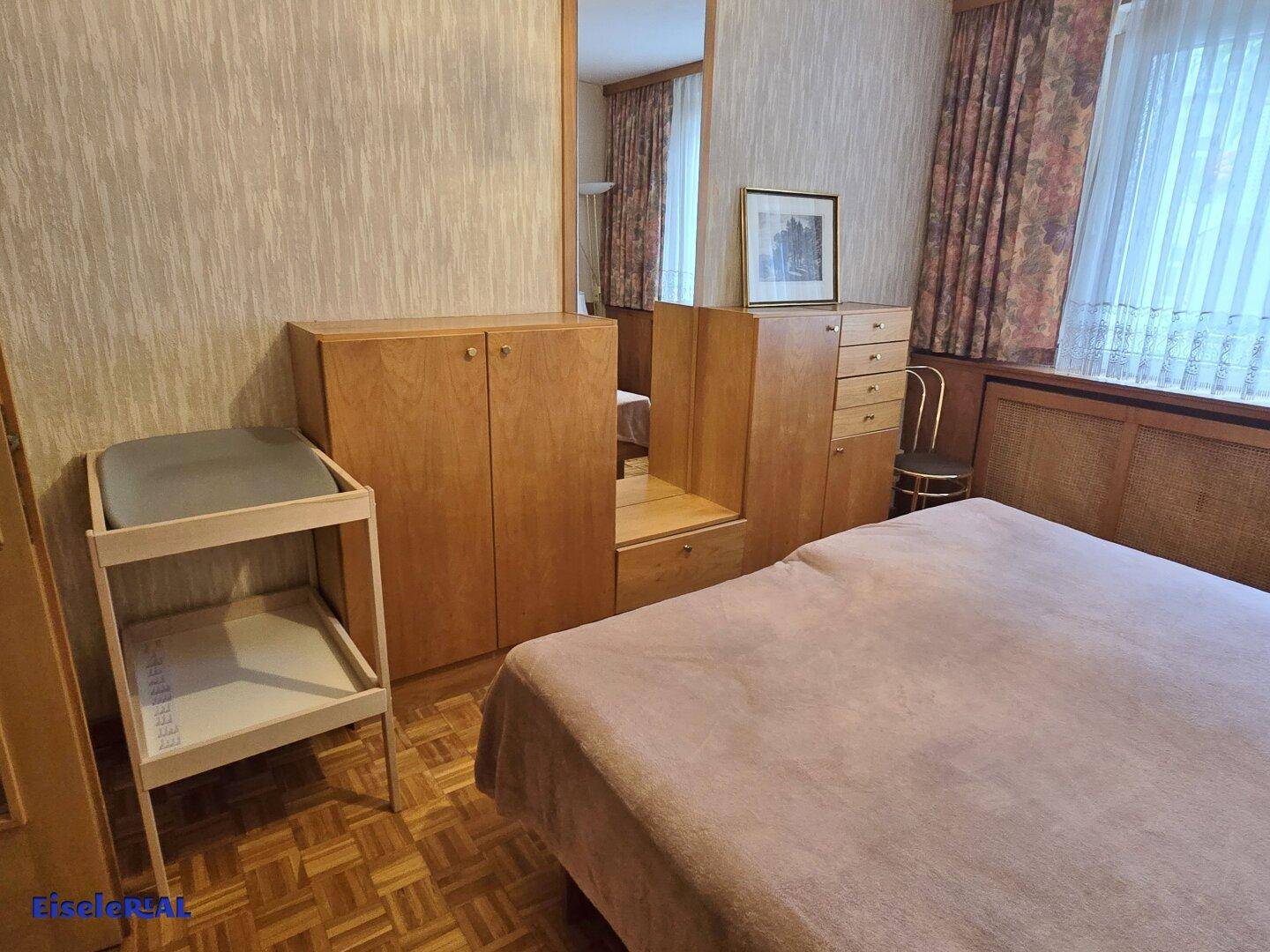 Schlafzimmer mit Einbauschränken aus Holz, einem Spiegel und traditioneller Einrichtung.