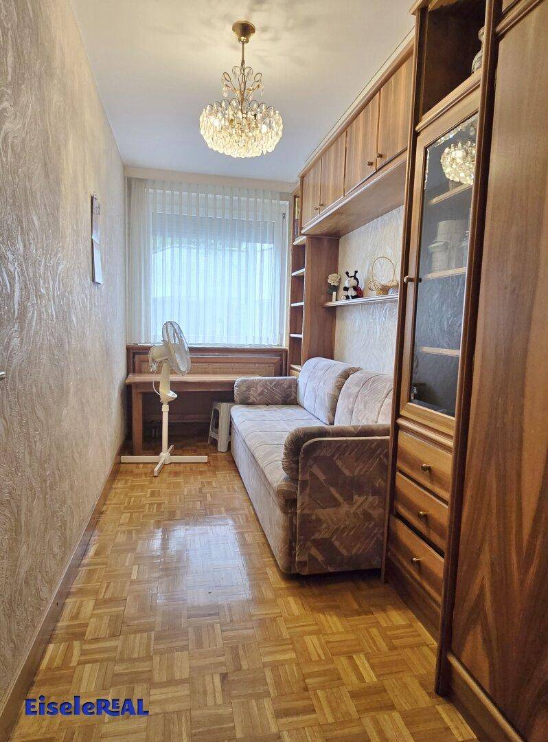 Kleineres Zimmer mit Sofa, Einbauregalen und Parkettboden, ideal als Gäste- oder Arbeitszimmer.
