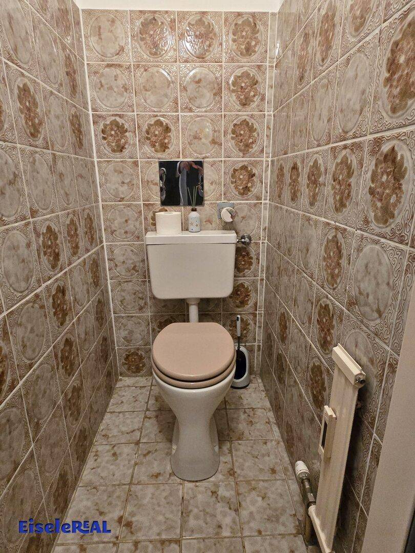 Separate Toilette mit gemusterten Wand- und Bodenfliesen und einem Heizkörper.