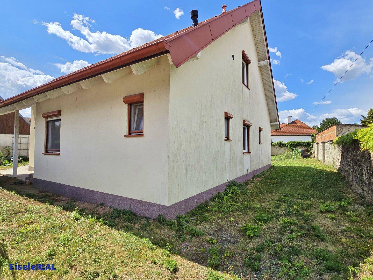 Seitenansicht des Hauses mit Gartenbereich unter blauem Himmel.