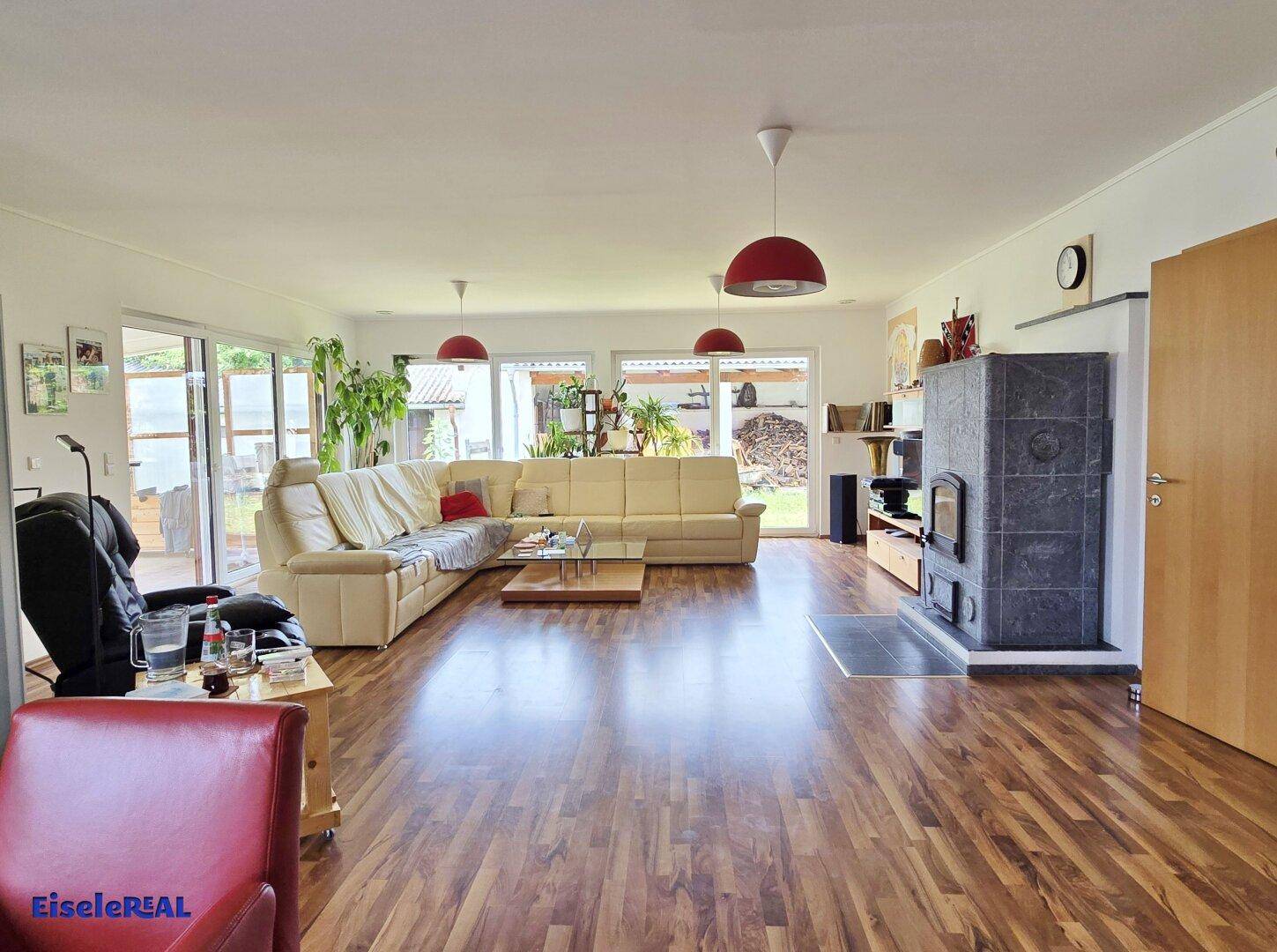 Geräumiges Wohnzimmer mit hellem Sofa, Holzboden und Kaminofen.