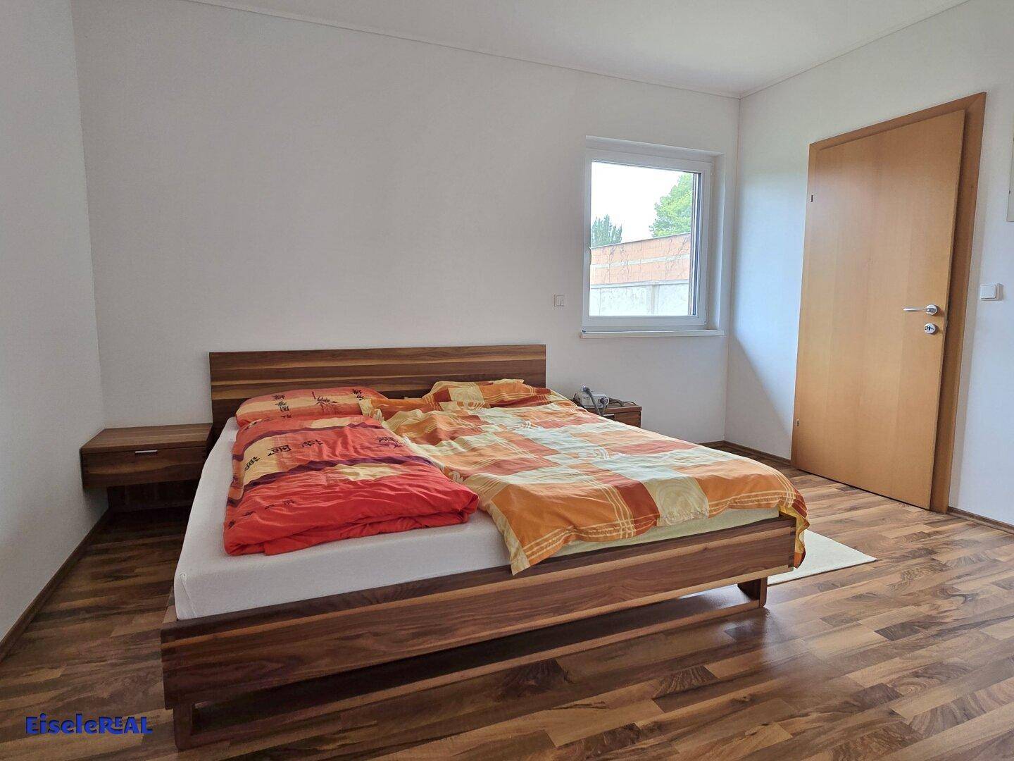 Schlafzimmer mit Holzbett, Nachttischen und Laminatboden.