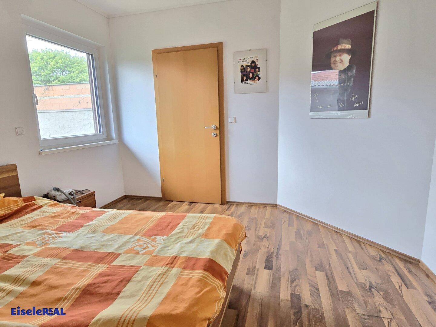 Helles Schlafzimmer mit Laminatboden und Fenster mit Blick ins Grüne.