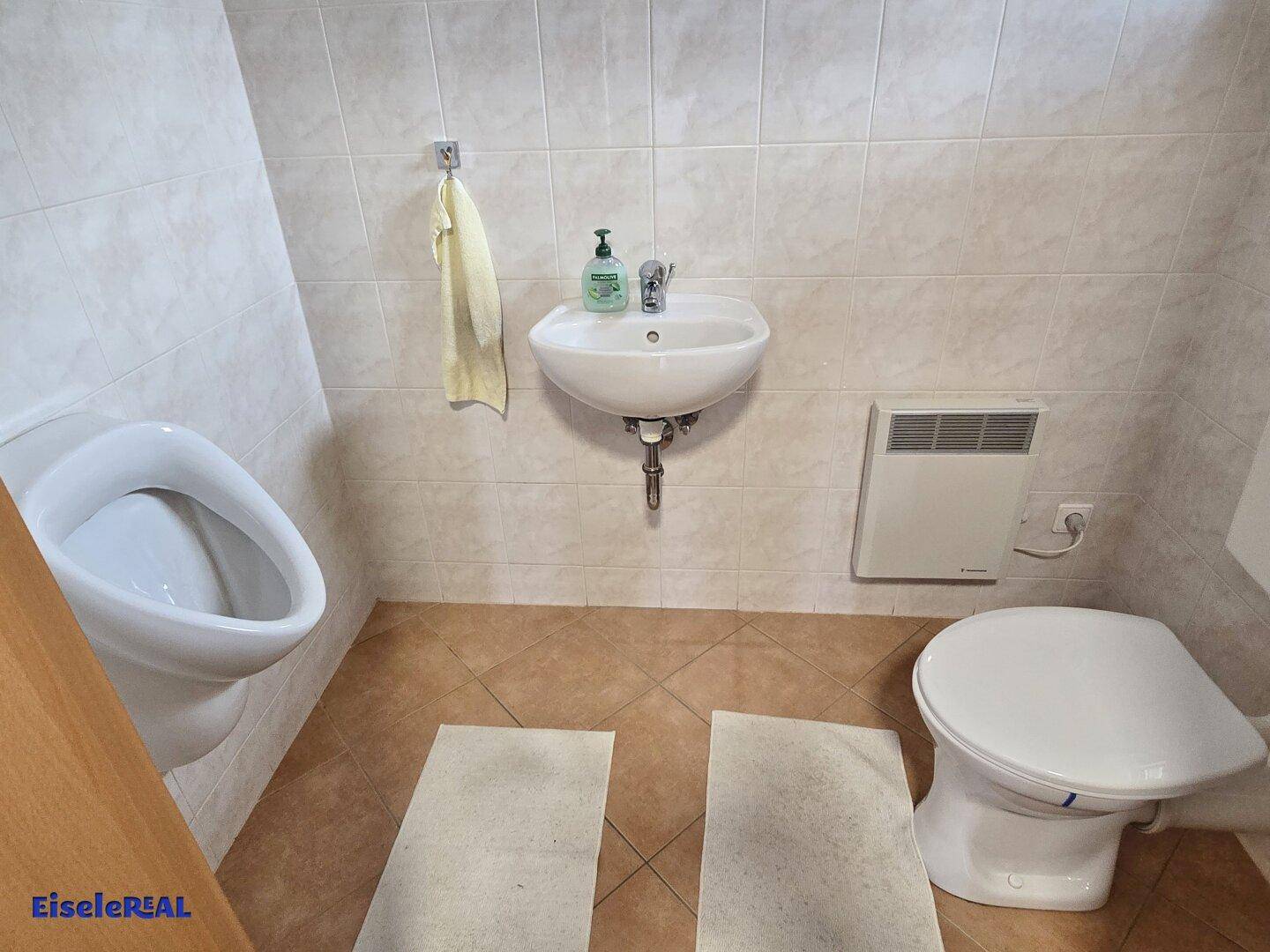 Gäste-WC mit Urinal, Waschbecken und Fliesen an Wänden und Boden.