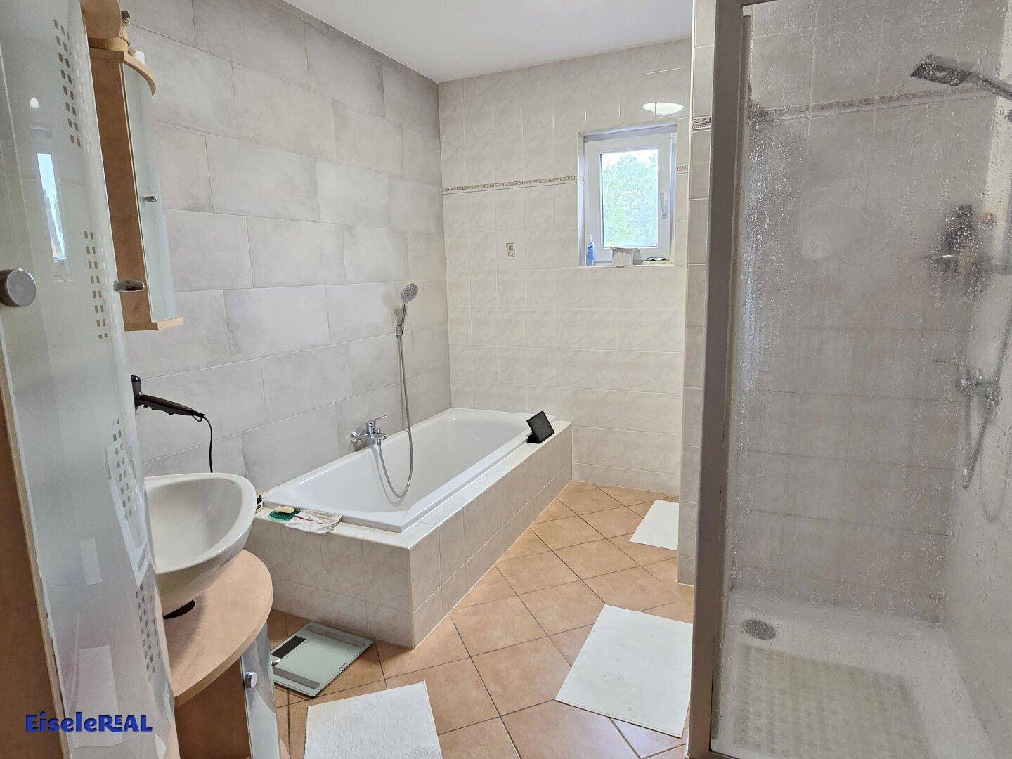 Badezimmer mit Badewanne, Duschkabine, Waschbecken und Fenster.