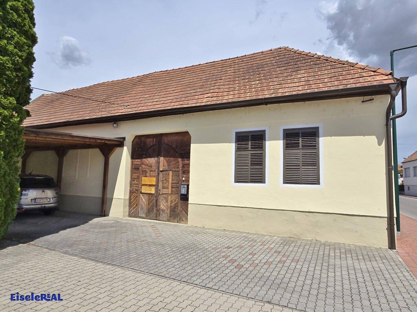Seitenansicht des Nebengebäudes mit Carport und Holztor.