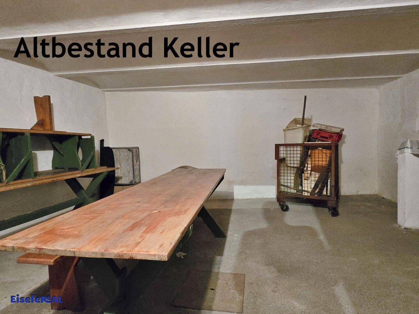 Geräumiger Kellerraum mit langem Holztisch, Regalen und einfacher Ausstattung, geeignet als Lager oder Werkstatt.