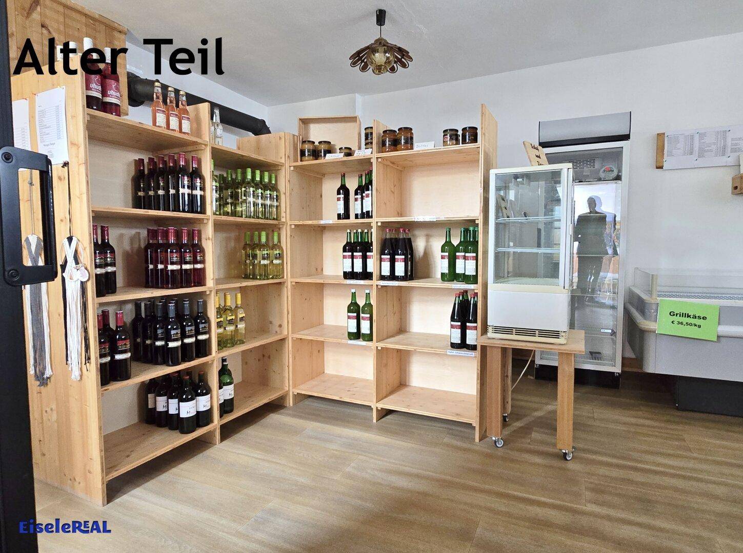 Raum mit Holzregalen voller Flaschen und Kühlgeräten, ideal für einen Hofladen oder zur Lagerung von Produkten.