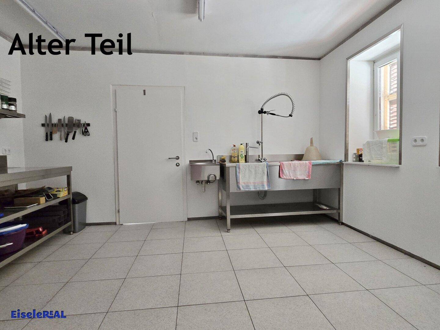 Funktionale Küche mit Edelstahlspüle, Arbeitsflächen und Fliesenboden, ideal für gewerbliche Nutzung.