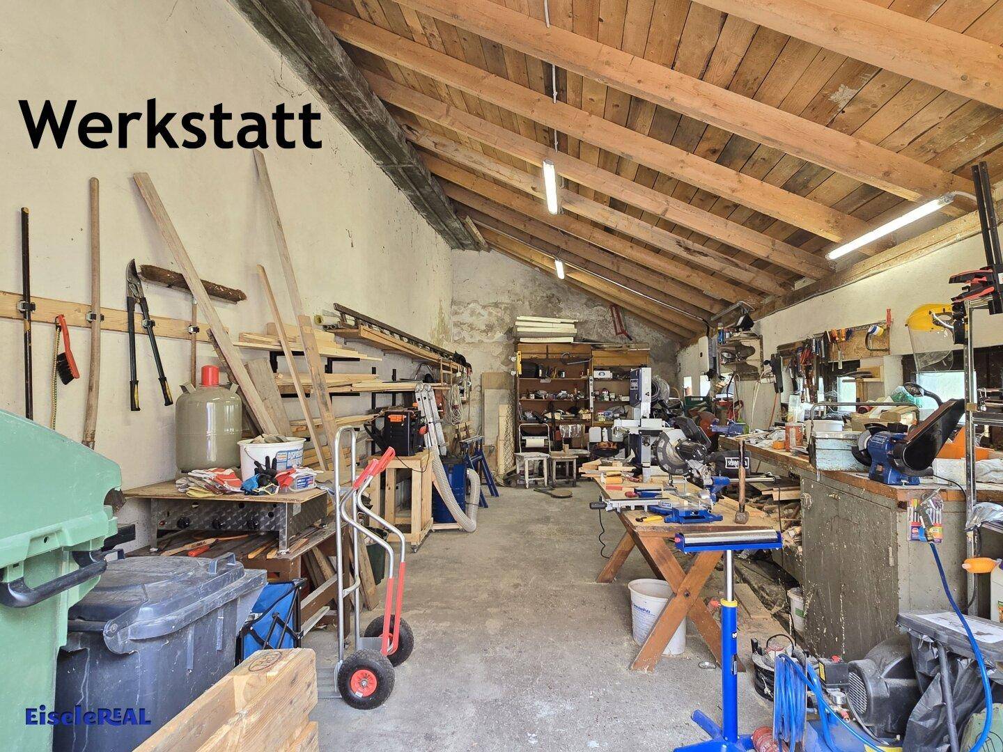 Geräumige Werkstatt mit sichtbaren Holzbalken, vielen Werkzeugen und Arbeitsflächen, ideal für Handwerker.