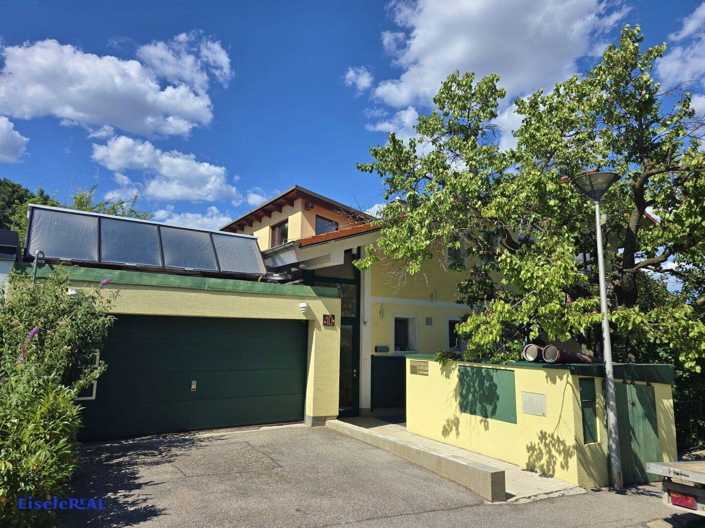 Vorderansicht des Hauses mit Garage, Solaranlage auf dem Dach und üppiger Vegetation.