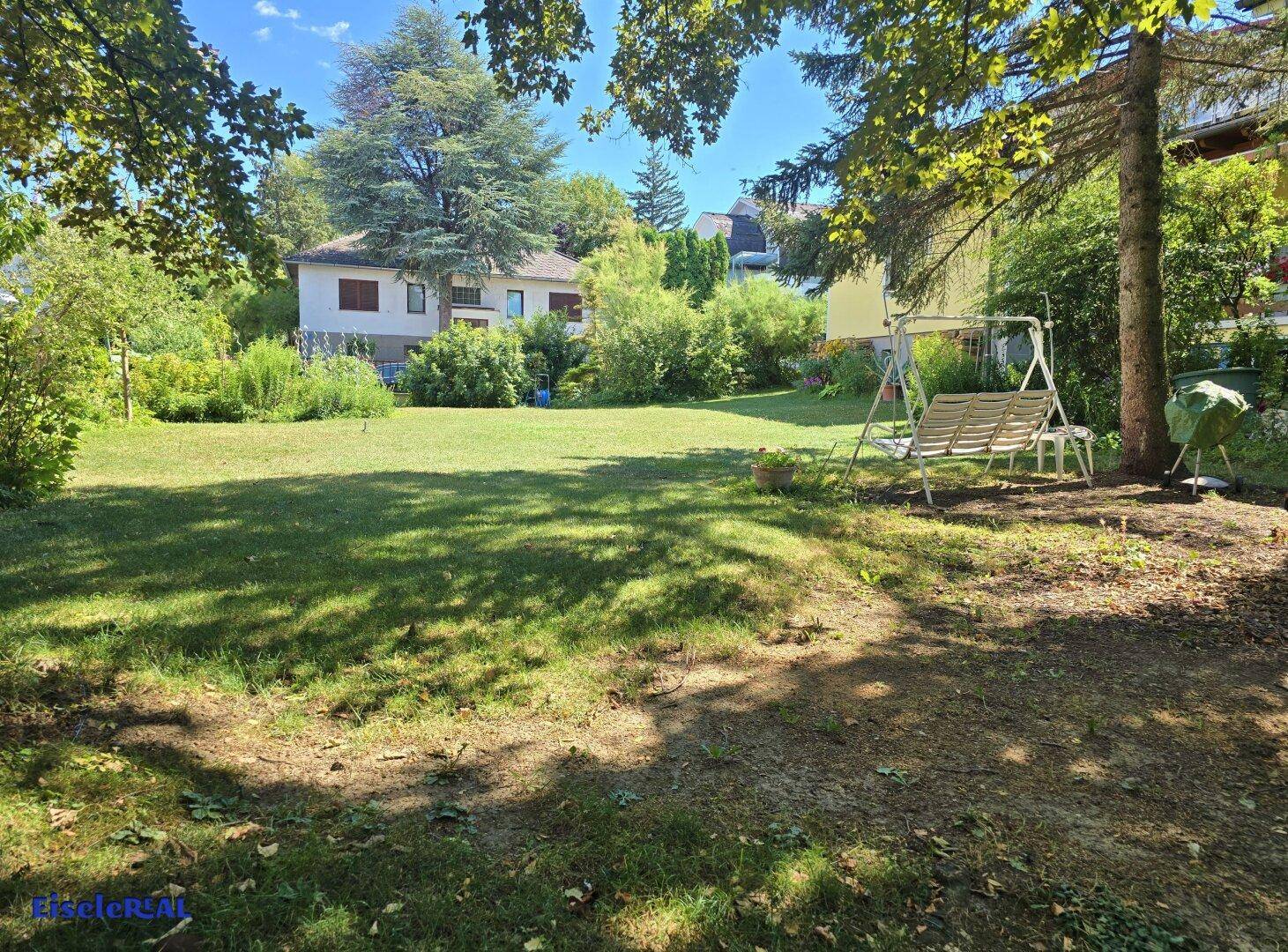 Weitläufige Rasenfläche im Garten mit Schaukel und altem Baumbestand.