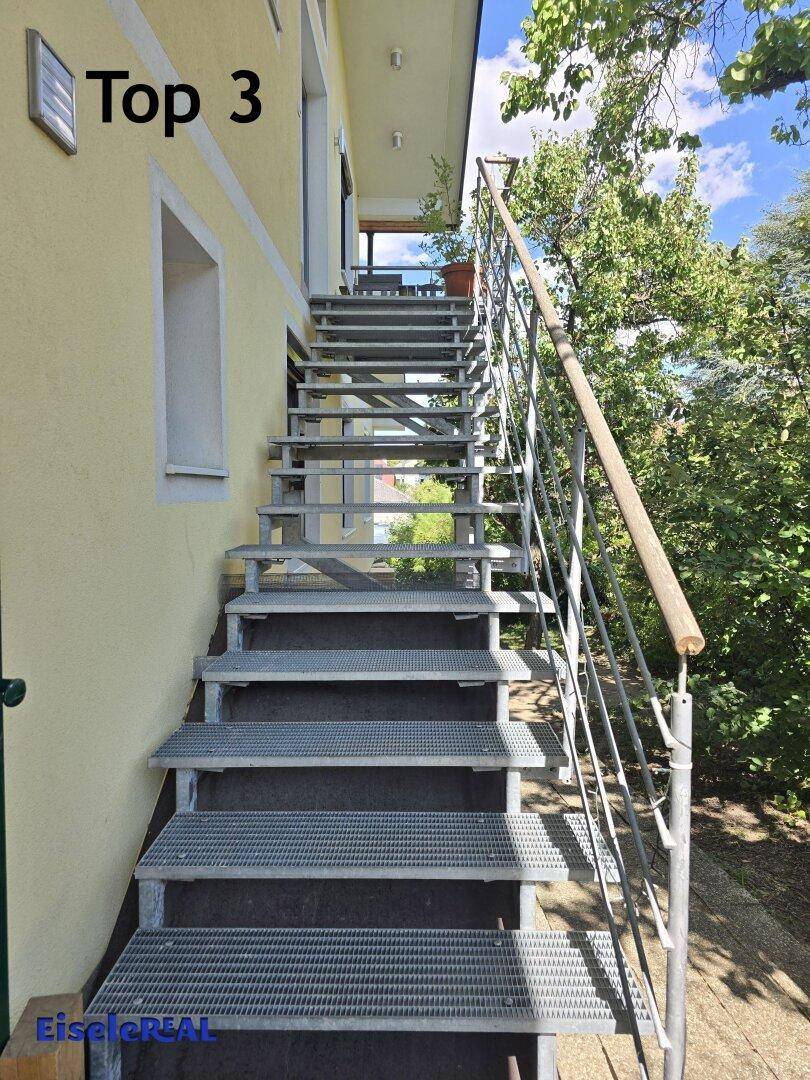 Außenliegende Metalltreppe mit Geländer, die zu einem oberen Stockwerk führt.