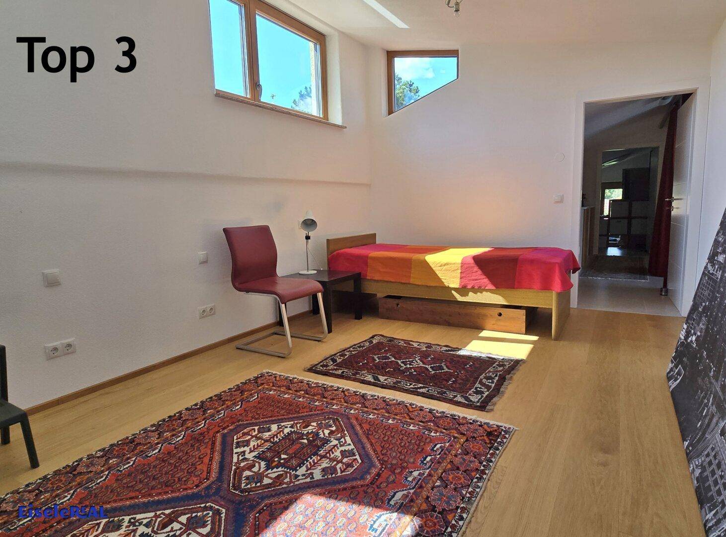Helles Schlafzimmer mit Holzboden, Einzelbett und großen Fenstern.