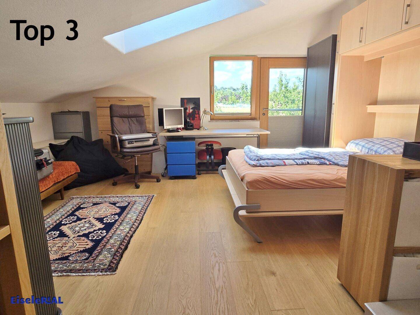Schlafzimmer mit Dachschräge, Schreibtischbereich und Zugang zu einem Balkon.