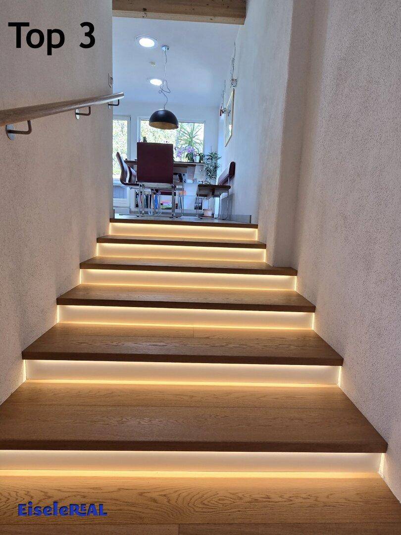 Moderne Holztreppe mit integrierter Beleuchtung, die zum Essbereich führt.