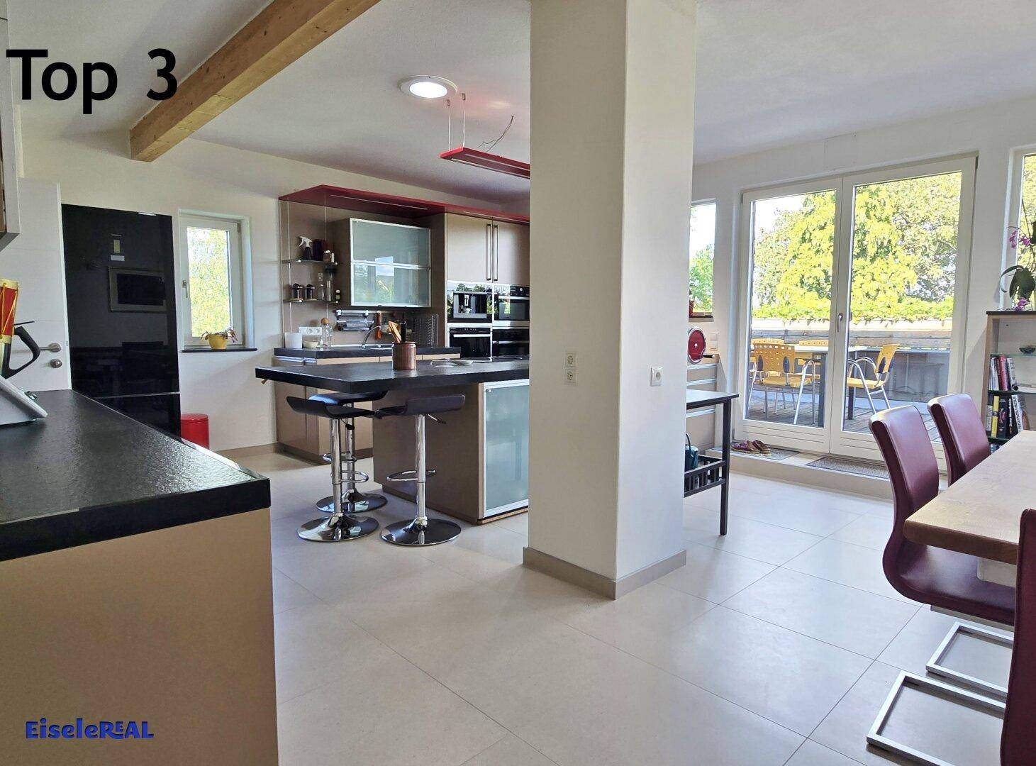 Offene Küche mit Kochinsel, Essbereich und großen Fenstern mit Zugang zur Terrasse.