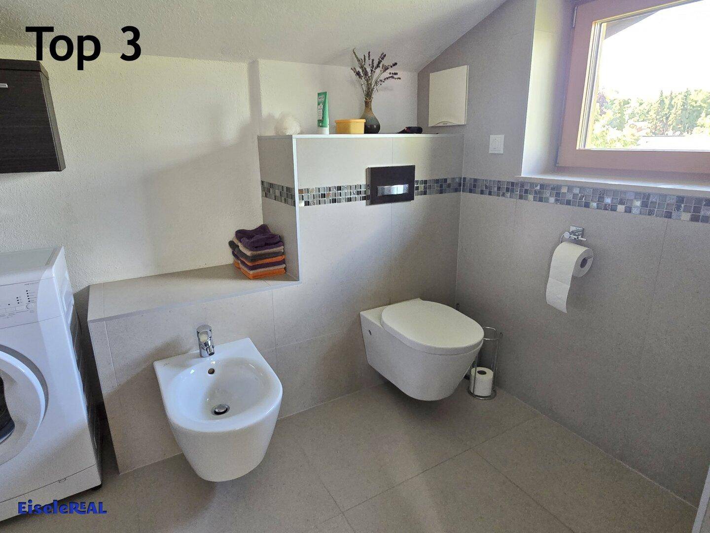 Helles Badezimmer mit Bidet, wandhängendem WC und Fenster, das für natürliche Belüftung sorgt.