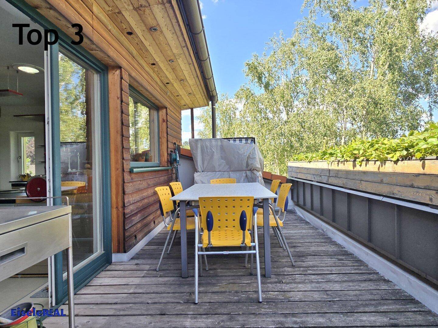 Holzterrasse mit Esstisch und Stühlen, umgeben von viel Grün und Bäumen für Privatsphäre.