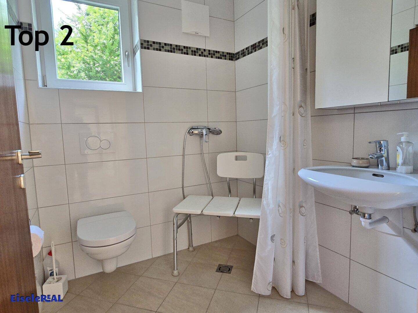 Barrierefreies Badezimmer mit Dusche, WC und Fenster, ausgestattet mit Haltegriffen und Duschsitz.