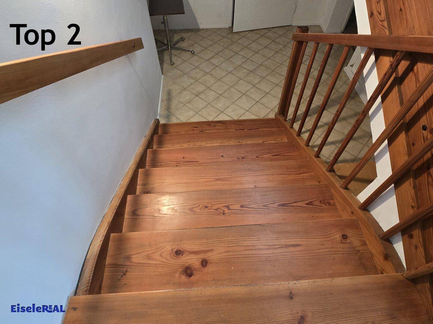 Holztreppe führt hinunter zu einem gefliesten Flur mit hellem Ambiente.
