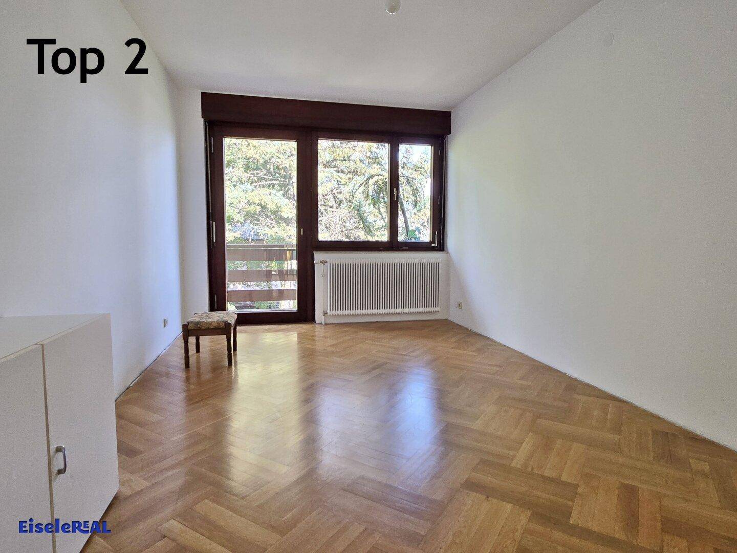 Helles Zimmer mit Parkettboden und großem Fenster, das Zugang zu einem Balkon bietet.