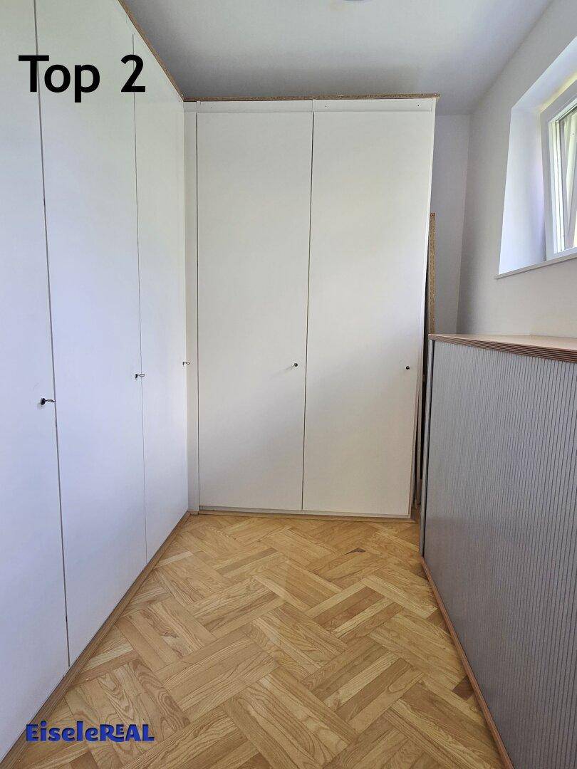 Praktischer begehbarer Kleiderschrank mit weißen Einbauschränken und Parkettboden.