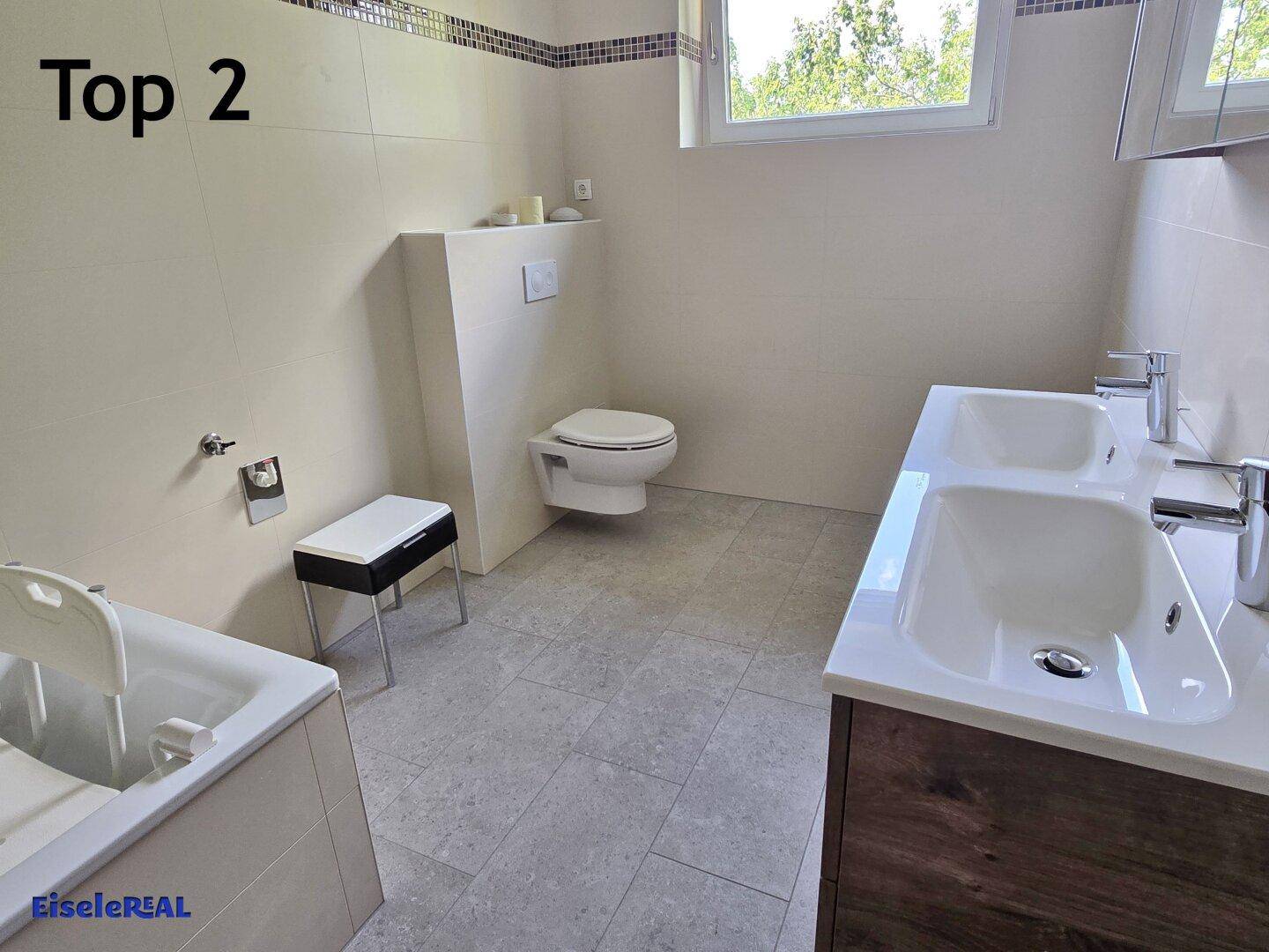 Helles Badezimmer mit Doppelwaschbecken, wandhängendem WC und Fenster.