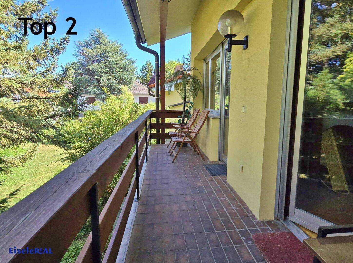 Geräumiger Balkon mit Fliesenboden, Holzgeländer und Sitzgelegenheiten im Grünen.