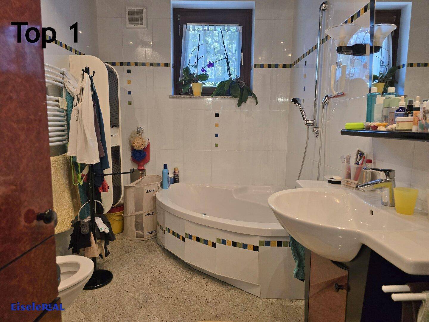 Badezimmer mit Eckbadewanne, Waschbecken, WC und farbenfrohen Fliesen.