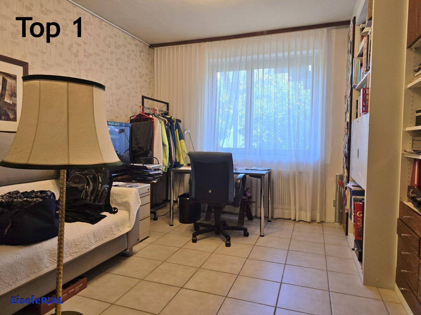 Funktionales Büro mit Fliesenboden, großem Fenster und umfangreichen Bücherregalen.