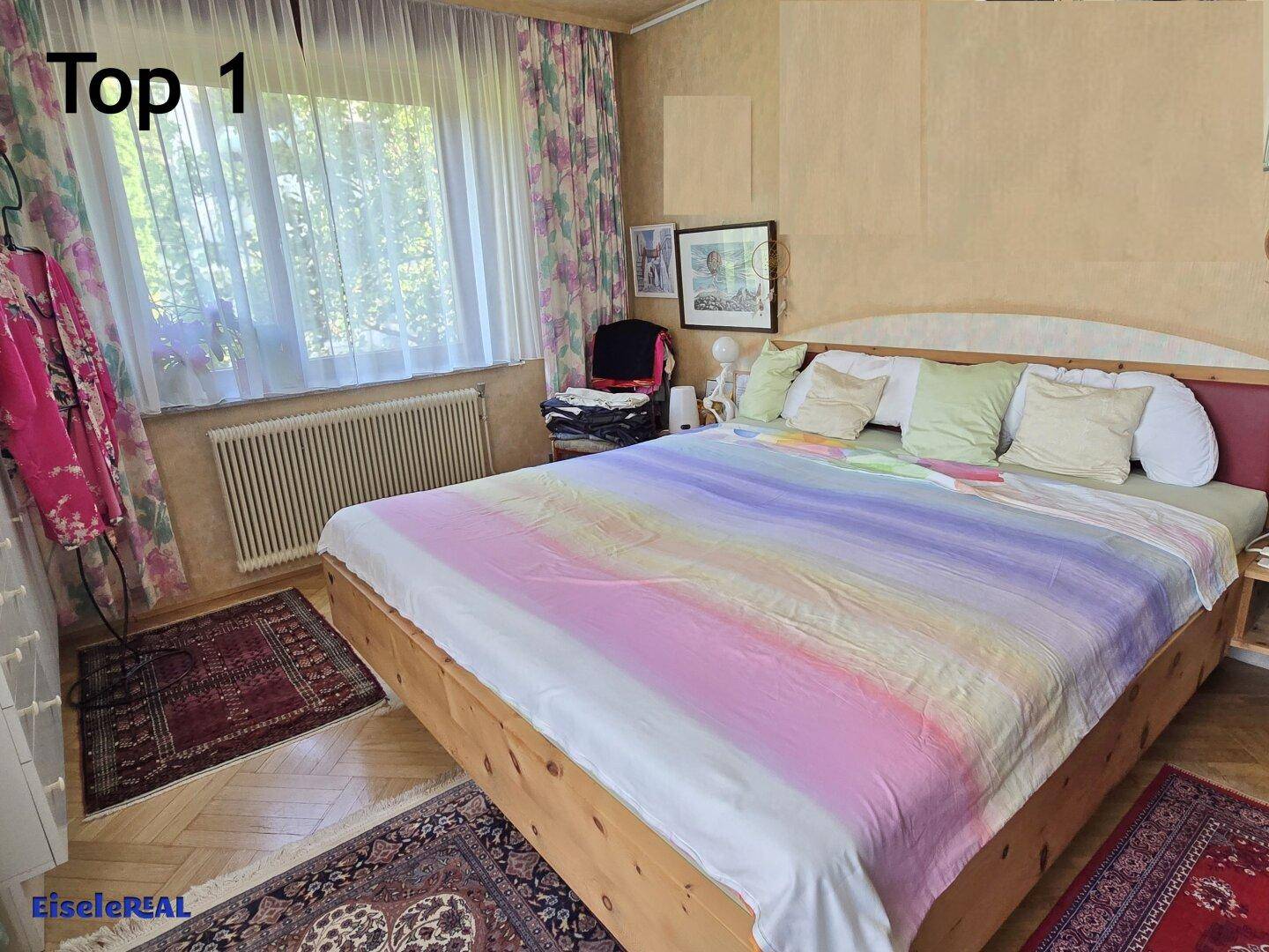 Gemütliches Schlafzimmer mit großem Bett, Parkettboden und Fenster mit Vorhängen.