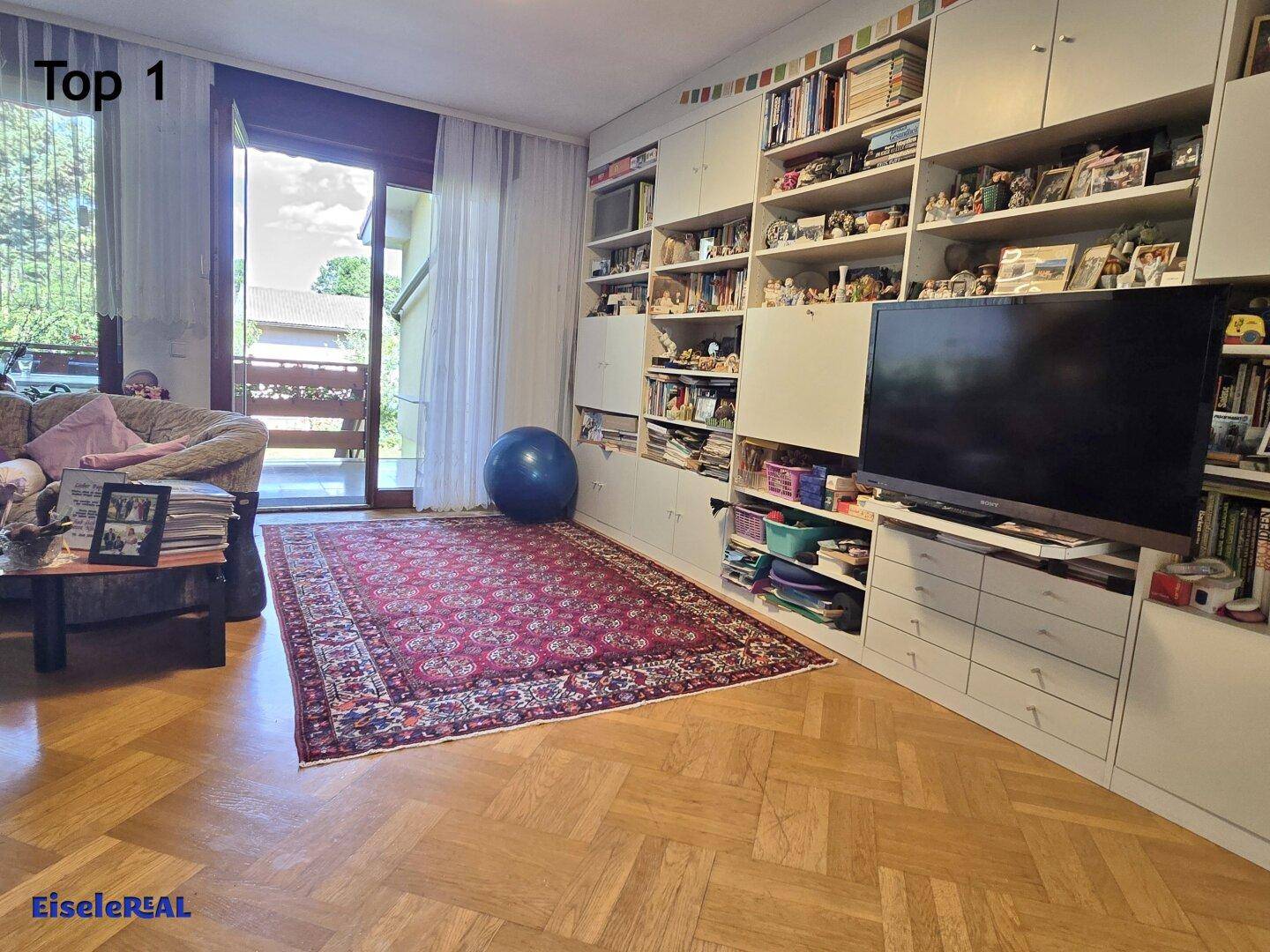 Helles Wohnzimmer mit Parkettboden, Einbauregalen und Zugang zum Balkon.